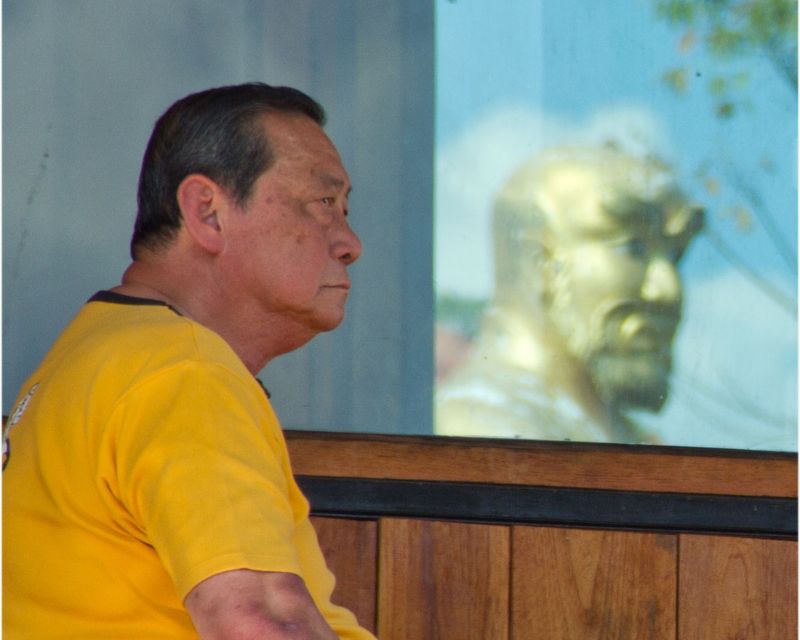 Grand Master Tan sitting at the tea table with Budhidharma statue in the background